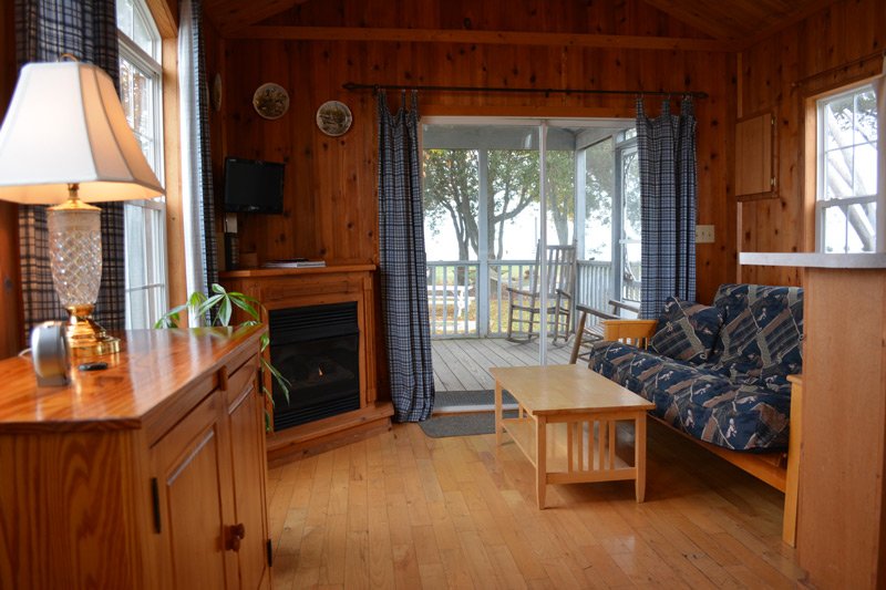 Interior of a wood-paneled cabin with a fireplace, a couch, a coffee table, and a sliding glass door leading to a deck at these Tilghman Island accommodations.