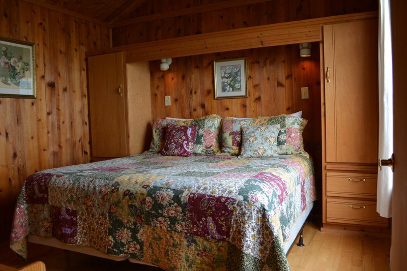 A bed with a floral patchwork quilt and several decorative pillows in a room with wood-paneled walls and built-in cabinetry, typical of Tilghman Island accommodations.